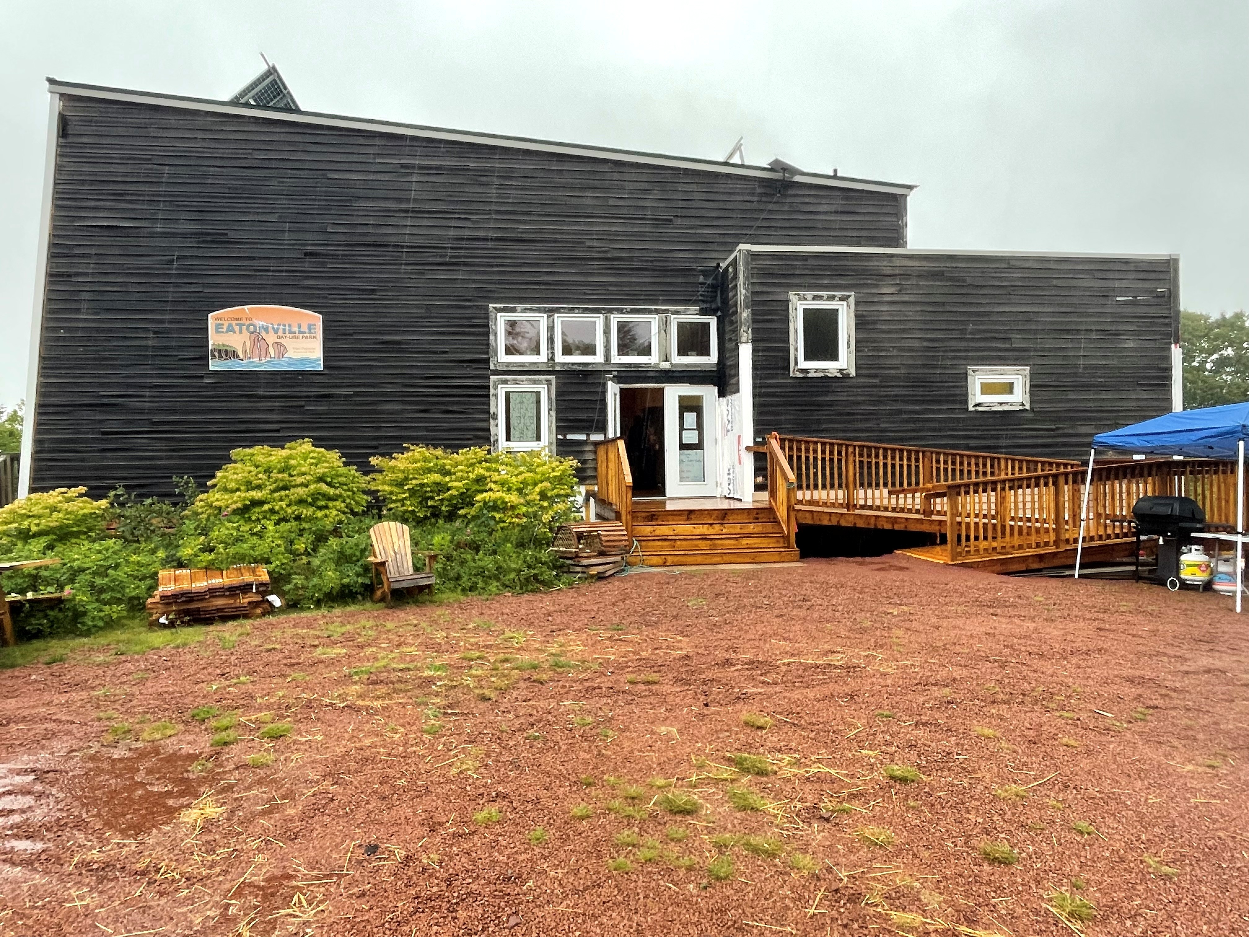 A black building with a gravel walkway during a cloudy, rainy day. It's home of the Three Sisters Interpretive Centre at the Cliffs of Fundy Global Geopark near Advocate Harbour.